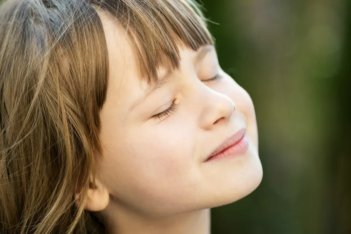 Criança de olhos fechados respirando pelo nariz ao ar livre