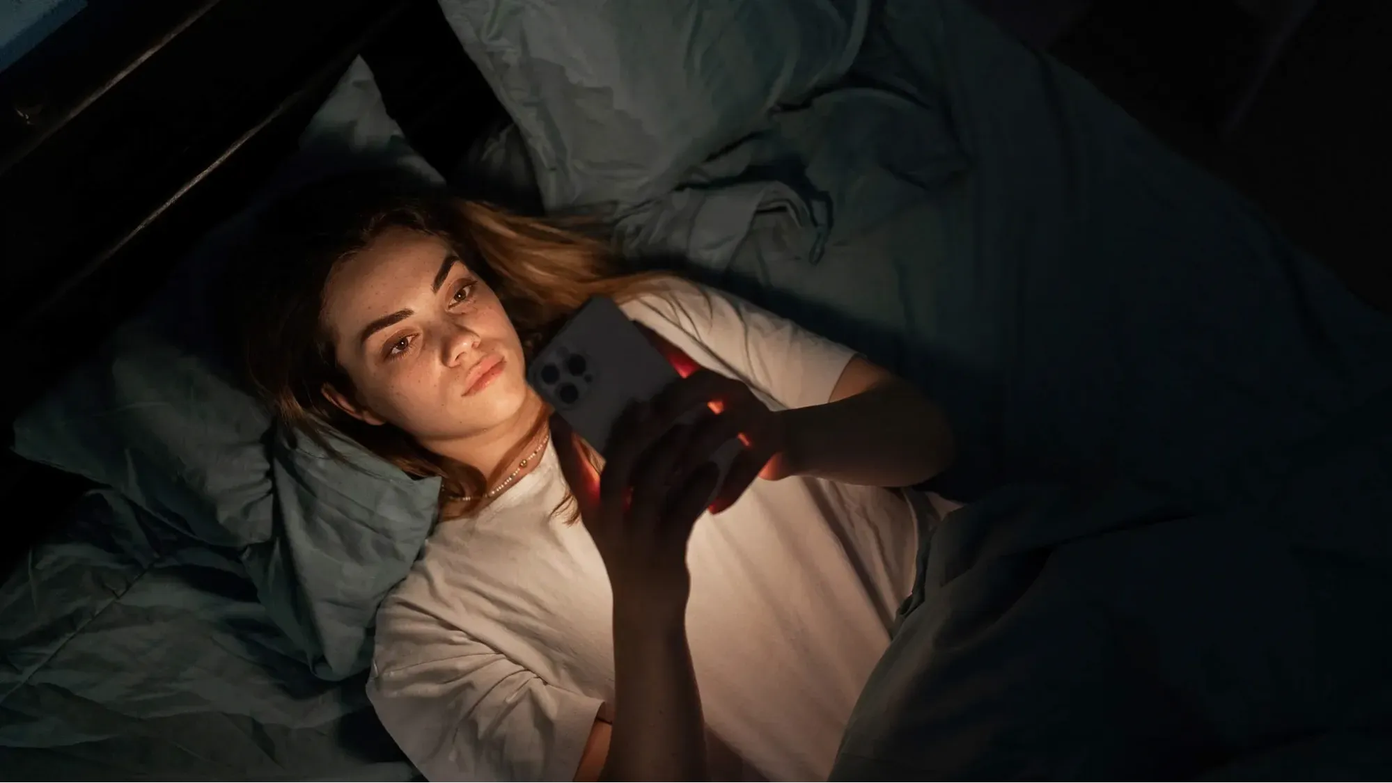 Pessoa deitada na cama à noite, com o rosto iluminado pela tela do celular