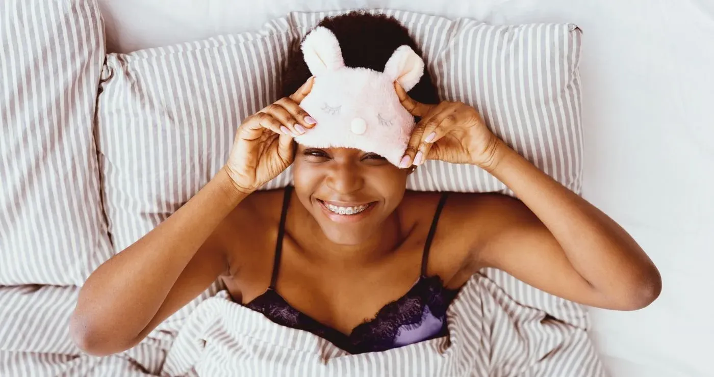 Pessoa acordando bem-disposta na cama, levantando a máscara de dormir