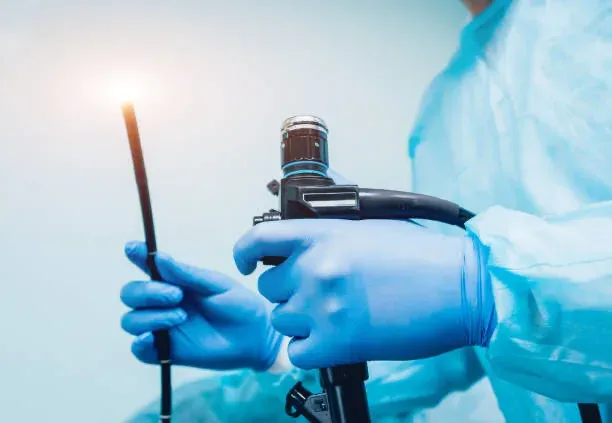 Mãos com luva segurando o fibroscópio flexível utilizado no exame